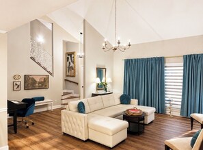 A living room with a sectional sofa, a desk, a chair, a chandelier, and a staircase.