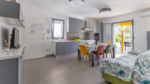 A modern kitchen with grey cabinets, a dining area with a table and chairs, and a bed with a tropical print bedspread. - White House Villa Luisa – Relax and Comfort Near the Beach (Santa Maria del Focallo)