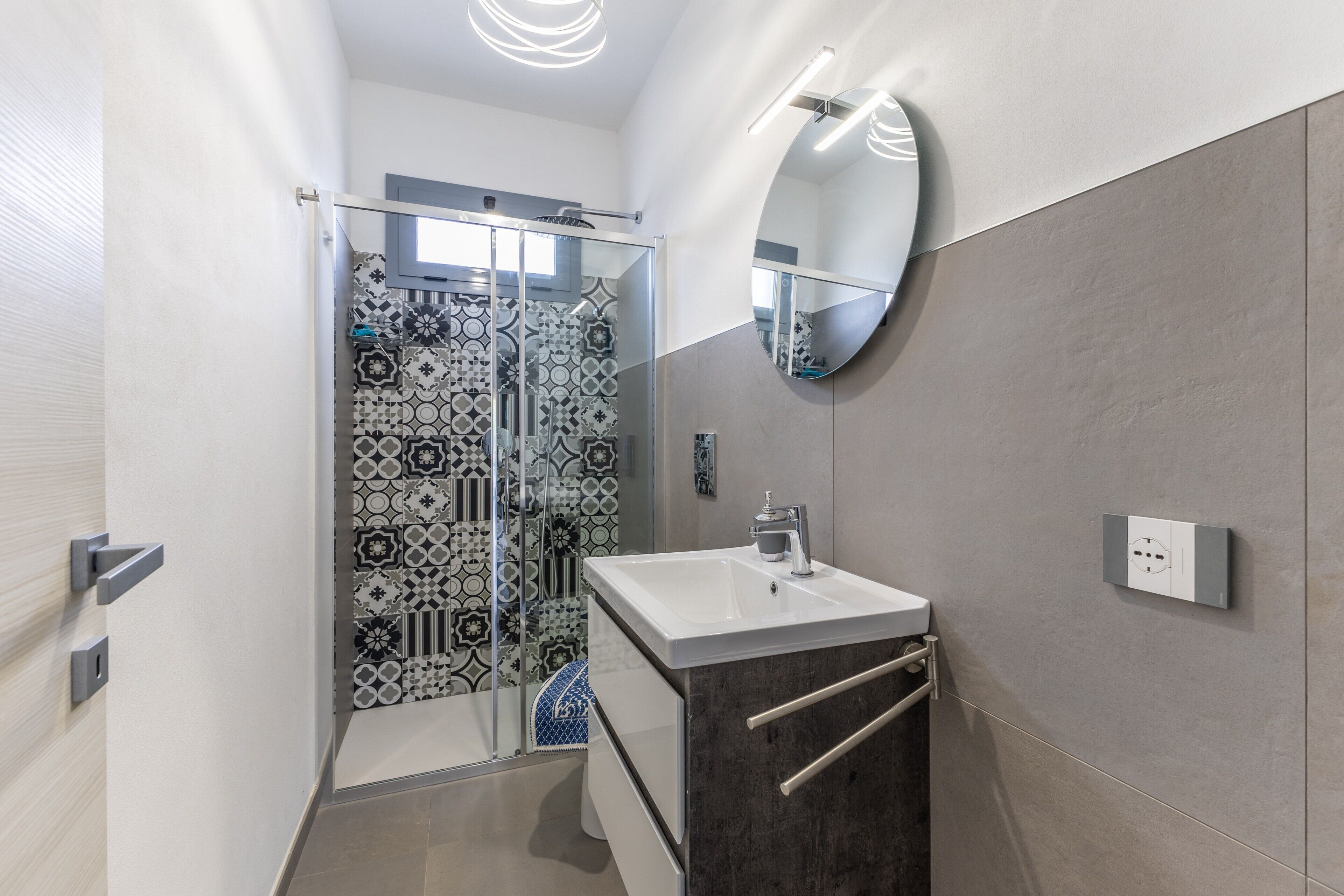 Une salle de bain moderne avec une douche à parois de verre, un lavabo blanc et un grand miroir.