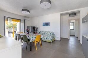 A modern kitchen with a dining area, a sofa, and a view of the outdoors.