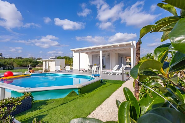 A swimming pool with a sun deck, lounge chairs, and a covered patio area.