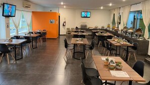 A modern dining area with multiple tables and chairs, a kitchen counter with food displays, and two televisions mounted on the walls. - Hotel Solé Plaza Guadalajara (Zapopan)