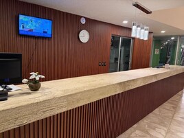 Un mostrador de recepción con una televisión, un reloj y un florero.
