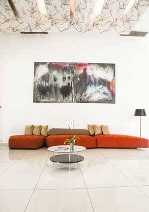 A modern living room with a large abstract painting, a red sofa, a coffee table, and a floor lamp. - Hotel Sole Plaza Guadalajara (Zapopan)