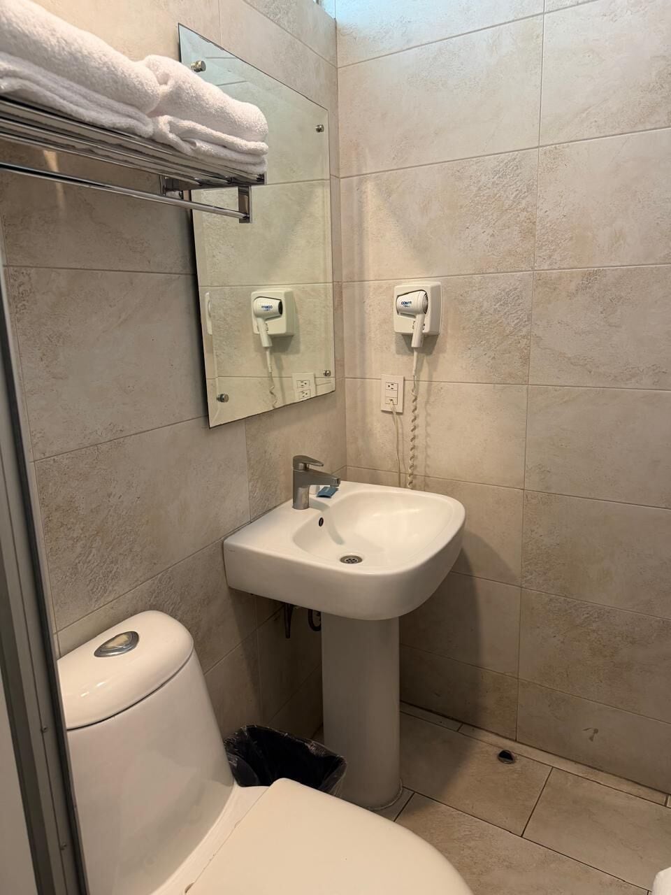 Et badeværelse med toilet, håndvask, bøjlestang til håndklæder og et spejl.