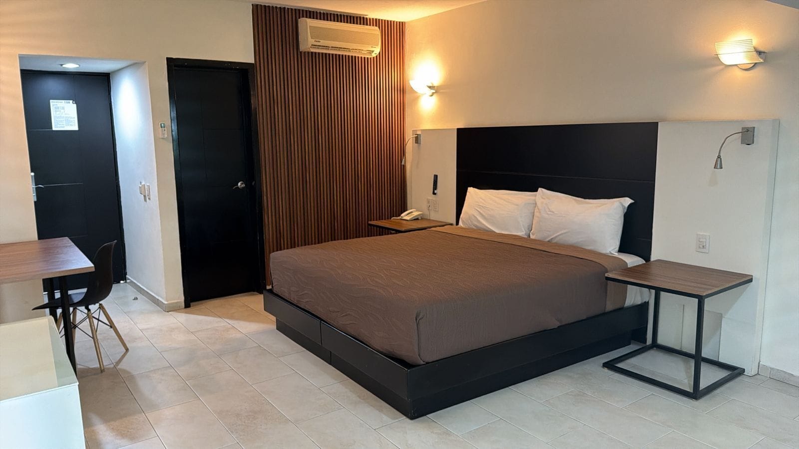Une chambre d’hôtel moderne dotée d’un grand lit, de tables de chevet, d’un appareil de climatisation et d’un mur revêtu de panneaux de bois.