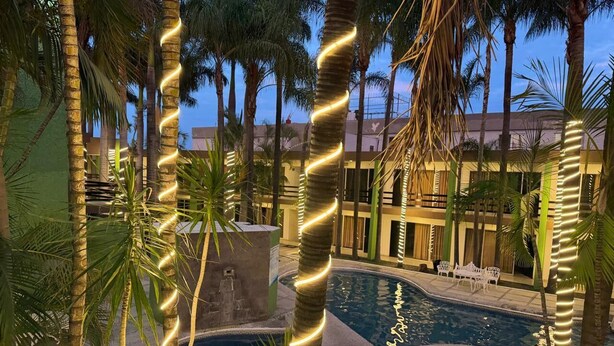 A pool area with palm trees, a stone structure, and a building in the background. - Hotel Solé Plaza Guadalajara (Zapopan)