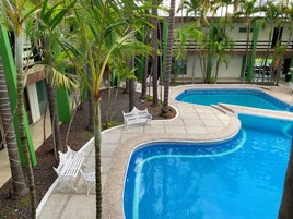 Una piscina de diseño curvo, rodeada de palmeras y mobiliario exterior blanco.