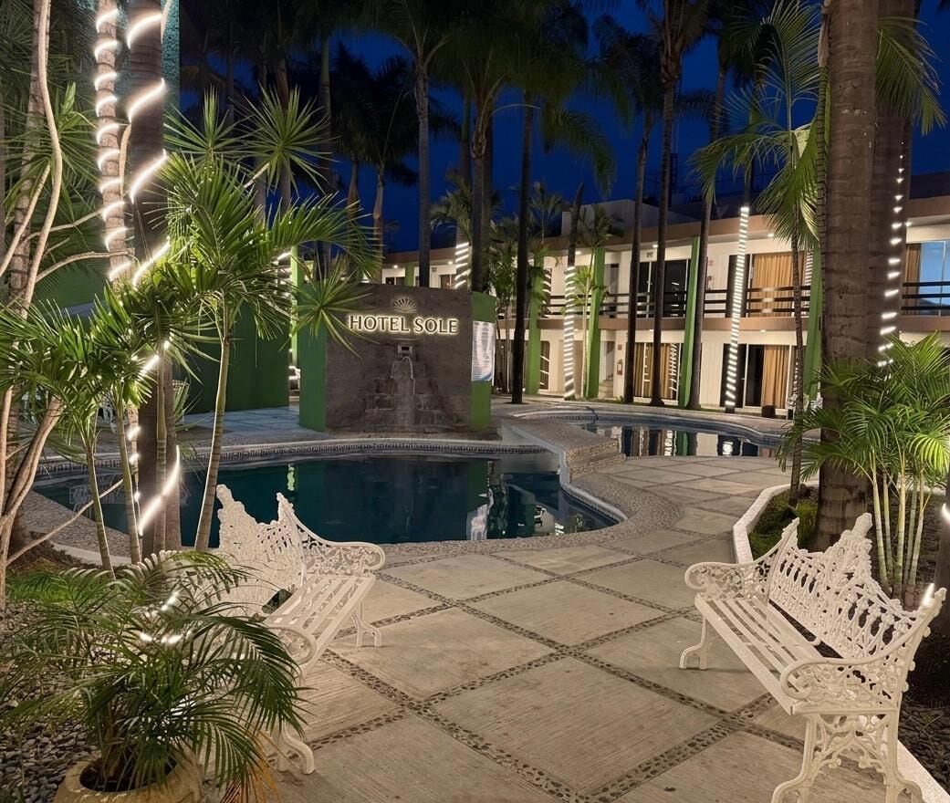 A hotel pool area with a sign reading 'HOTEL SOLLE,' surrounded by palm trees and benches.