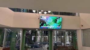 A hotel entrance with a large TV screen displaying an advertisement, glass doors, and a modern interior design. - Hotel Solé Plaza Guadalajara (Zapopan)