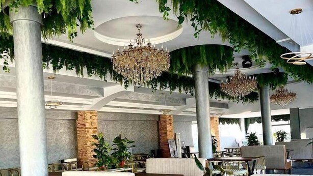Un comedor interior con mesas y sillas de madera, plantas colgantes y candelabros.