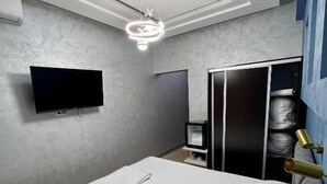 Un dormitorio con cama, televisión, armario y luz de techo.