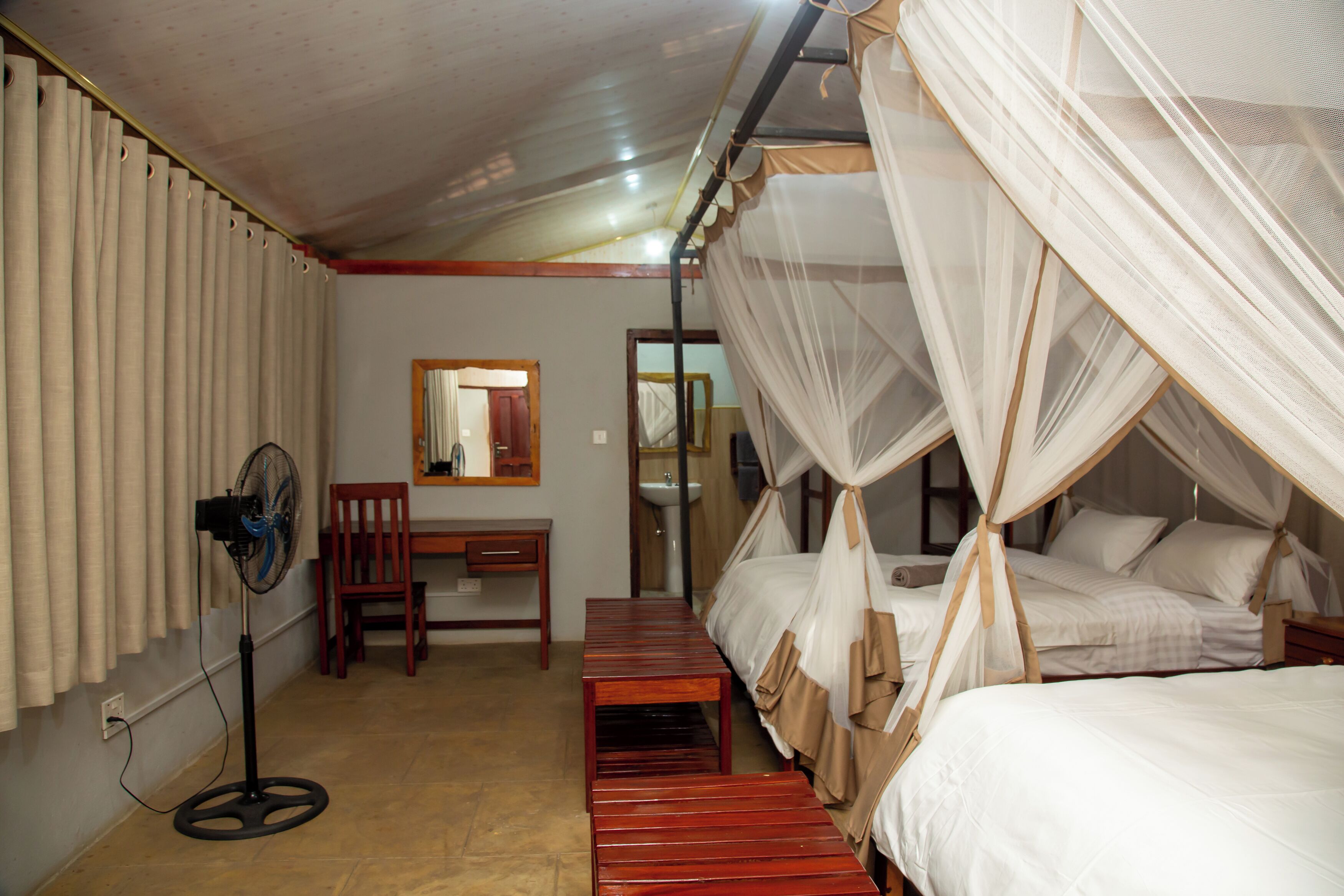 A room with a bed, a desk, a chair, a fan, and a mirror.