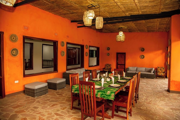 A dining area with a table set for six, surrounded by wooden chairs, and a sofa in the background.