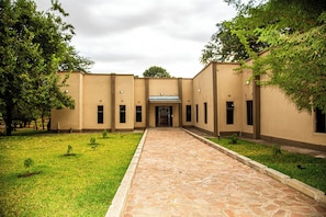 A building with a central entrance, a paved walkway, and a grassy area with small plants.