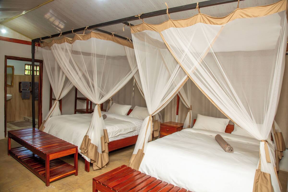 A room with two beds, each with a canopy, wooden benches, and a small table.