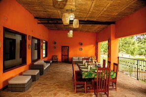 An outdoor dining area with wicker furniture, a stone floor, and a view of greenery.