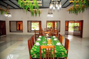 A dining area with a table set for four, surrounded by chairs, with hanging plants and a ceiling light fixture.