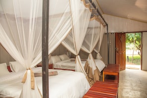 Quarto com quatro camas, cada uma com dossel, e um banco de madeira.