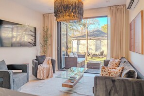 Een moderne woonkamer met een glazen salontafel, grijze banken en een groot raam met gordijnen.