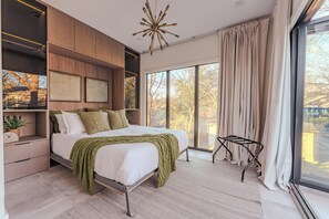 A modern bedroom with a large bed, built-in storage, a unique ceiling light, and a view through large windows. - FIFA 2026 HQ - Two Cabins, Sleeps 12 - 2.5 Mi to Mercedes-Benz Stadium (Atlanta)