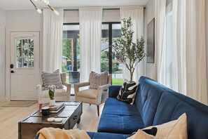 A living room with a blue sofa, a white door, and a view of the outdoors. - FIFA 2026 HQ - Two Cabins, Sleeps 12 - 2.5 Mi to Mercedes-Benz Stadium (Atlanta)