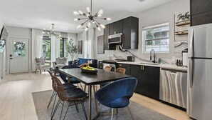 Eine moderne Küche mit dunklen Schränken, einem Edelstahlkühlschrank und einem Essbereich mit einem schwarzen Tisch und blauen Stühlen.