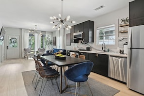 A modern kitchen with dark cabinets, a stainless steel refrigerator, and a dining area with a black table and blue chairs. - FIFA 2026 HQ - Two Cabins, Sleeps 12 - 2.5 Mi to Mercedes-Benz Stadium (Atlanta)