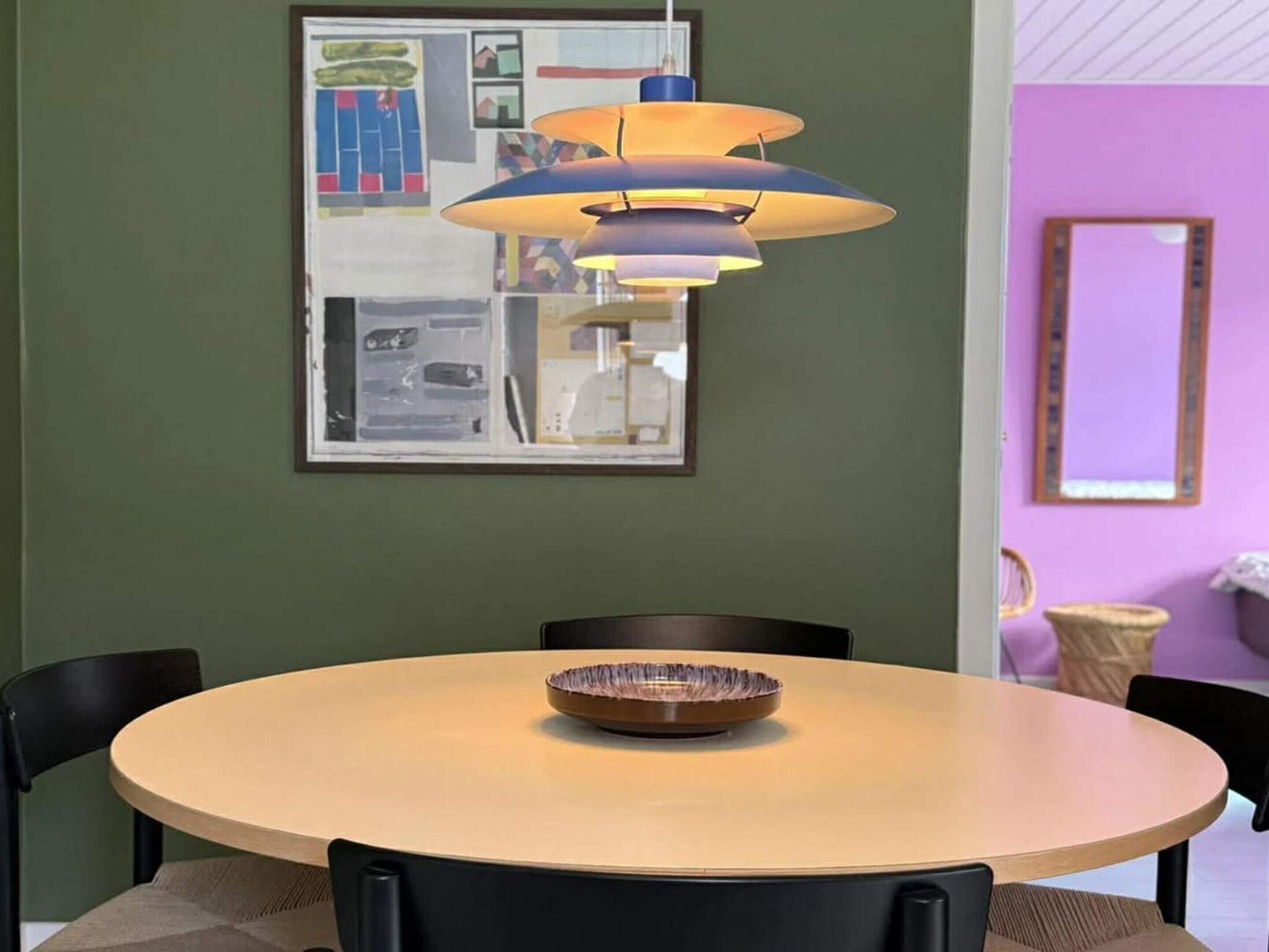 A round dining table with a bowl in the center, surrounded by chairs, under a multi-tiered pendant light.
