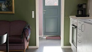 Huoneessa on sohva, kahvinkeitin ja ovi, joka johtaa toiseen huoneeseen.