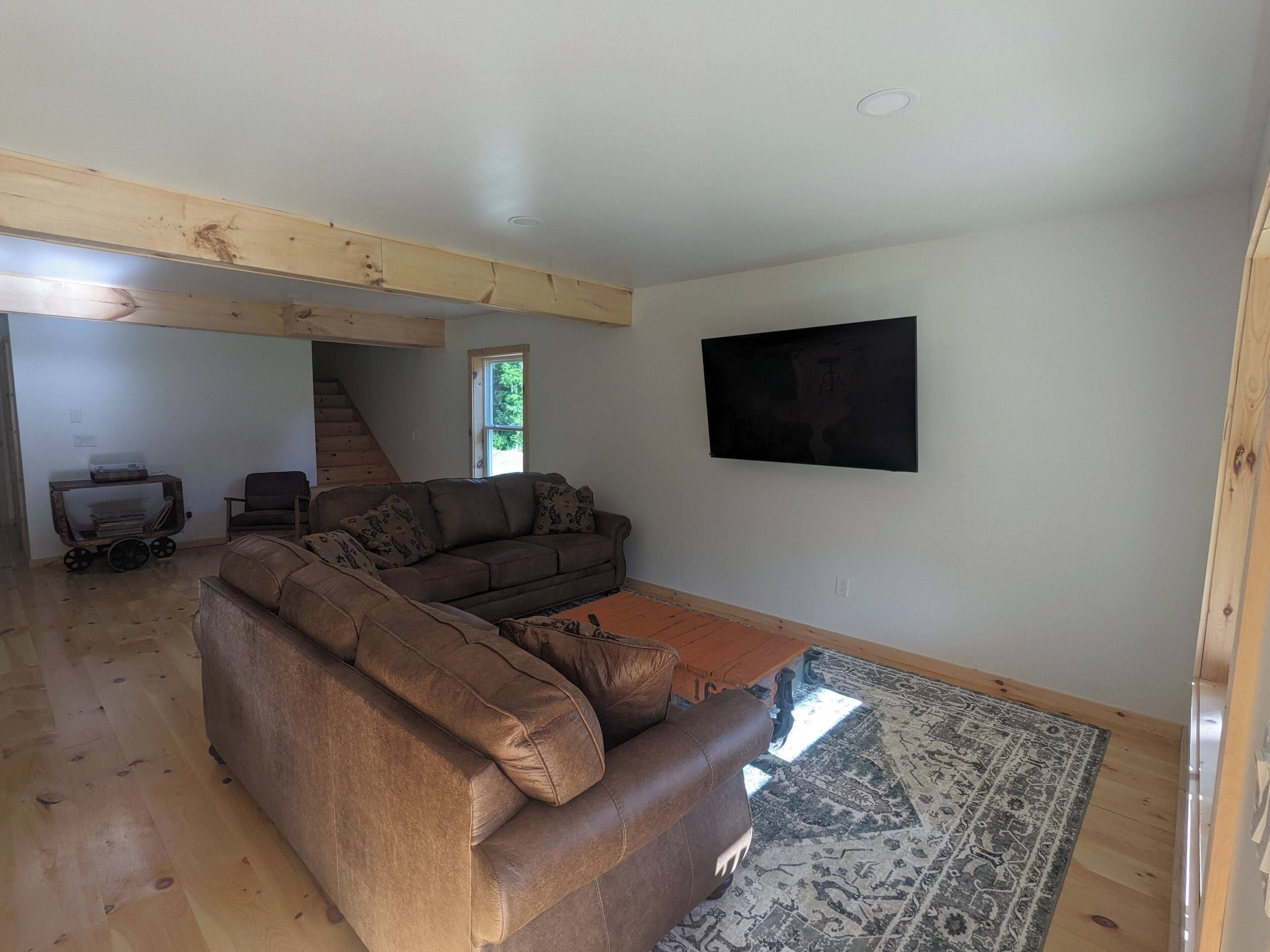 Een ruime woonkamer met een hoekbank, een flatscreen televisie aan de wand en een houten vloer.