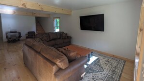 A spacious living room with a sectional sofa, a flat-screen TV mounted on the wall, and a wooden floor. - The Cabins at Timber Ridge - 6 Cabin Group Retreat - Weddings, Reunions, Clubs (Tamworth)