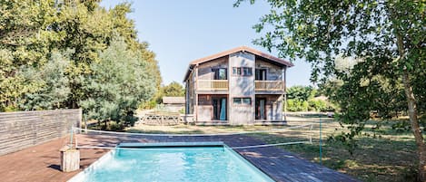 Una casa de madera de dos pisos con una piscina delantera.