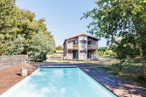 A two-story wooden house with a swimming pool in front.