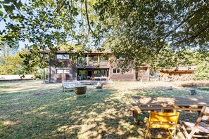 Een houten huis met terras, zitplaatsen buiten en een gazon.
