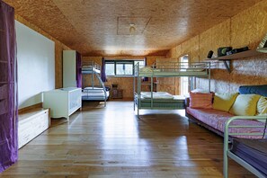 A room with bunk beds, a sofa, a window, and wooden walls.