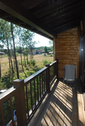 Eine Holzterrasse mit Geländer, einem Klappstuhl und Blick auf ein Grasfeld und Bäume.