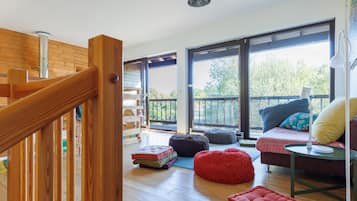 Un'ampia stanza con una scala in legno, ampie finestre e un angolo relax con cuscini.