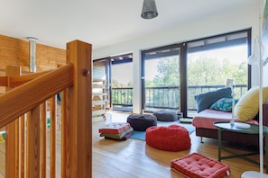 A spacious room with a wooden staircase, large windows, and a cozy seating area with cushions.