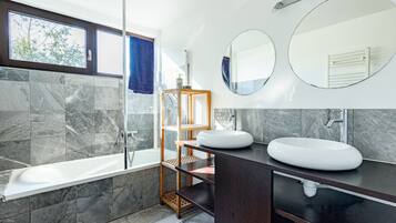 Een moderne badkamer met een bad, twee wasbakken, een douche en een grote spiegel.