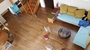 Une pièce avec un plancher en bois, un canapé avec des coussins, une petite table, une chaise et un tabouret décoratif.