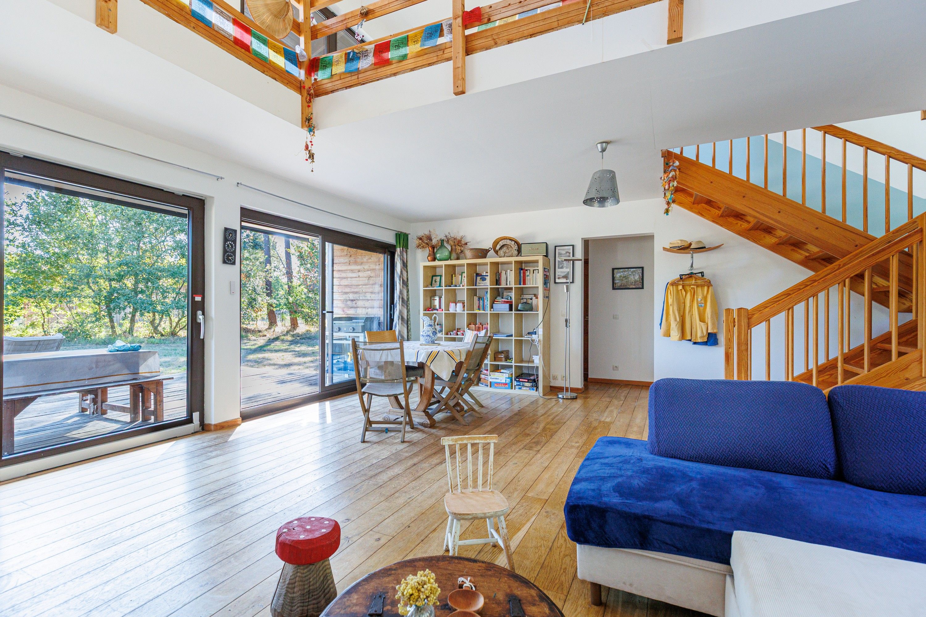 Un'ampia zona giorno con una scala in legno, un divano blu, una libreria e un tavolo da pranzo.