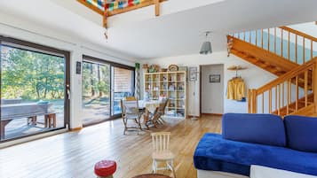 Een ruime woonruimte met een houten trap, een blauwe bank, een boekenkast en een eettafel.