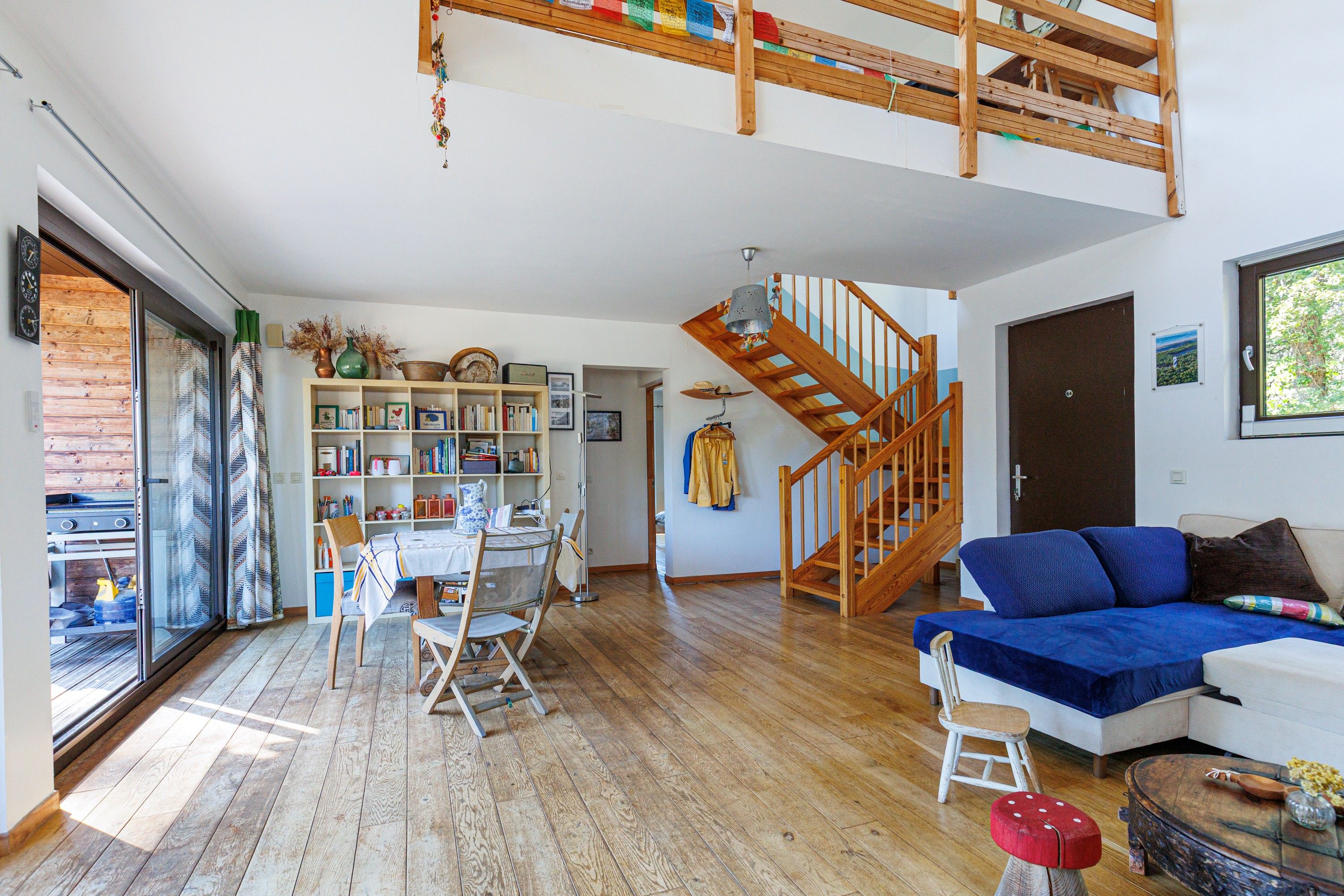 Un vaste espace de vie agrémenté d’un escalier en bois, d’un canapé bleu et d’une bibliothèque remplie de livres et d’objets décoratifs.