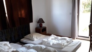 Une chambre avec deux lits simples, une table de chevet avec une lampe, une chaise et une vue sur l’extérieur par une fenêtre.