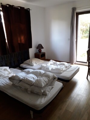 Ein Zimmer mit zwei Einzelbetten, einem Nachttisch mit Lampe, einem Stuhl und Blick durch ein Fenster.