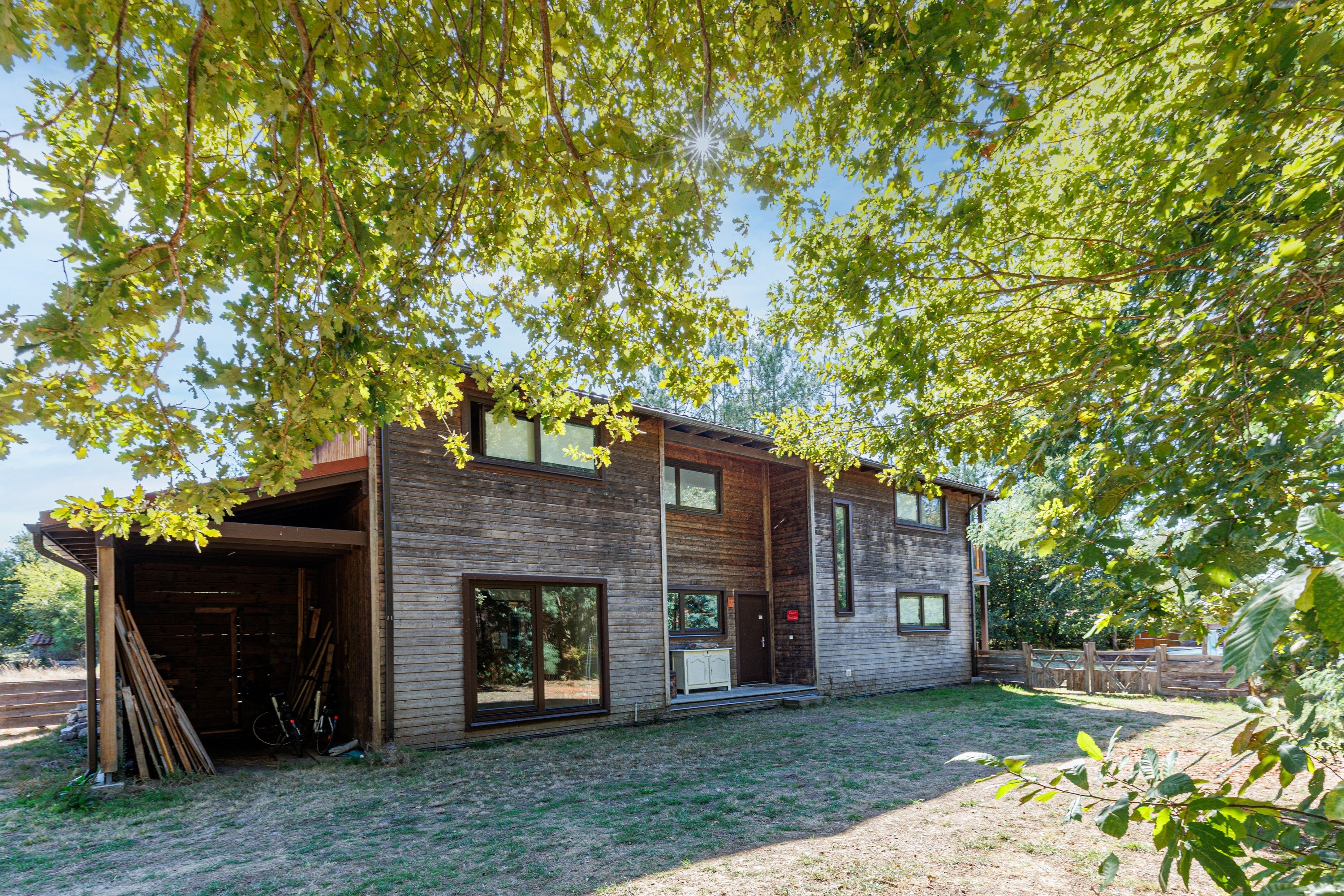 Une maison moderne à deux étages, dotée d’un grand garage ouvert et d’un espace extérieur abrité.