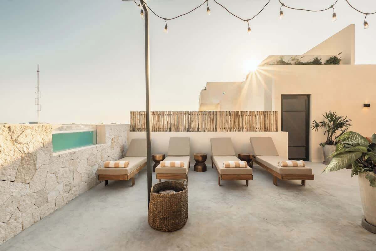 A rooftop lounge with sun loungers, a small pool, and string lights.