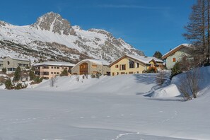 Ein verschneites Bergresort mit mehreren Gebäuden, darunter ein Steinhaus und ein gelbes Gebäude mit großen Fenstern.