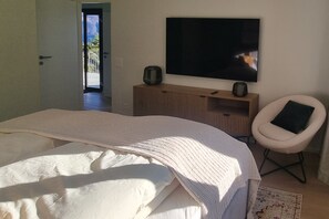 A bedroom with a bed, a TV, a chair, and a door leading to a balcony. - Villa Chiara – House with Pool & Garden Near Lake Maggiore (Brissago)